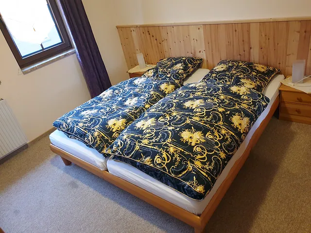 Schlafzimmer mit Doppelbett vor einer Holzrückwand aus Zirbe