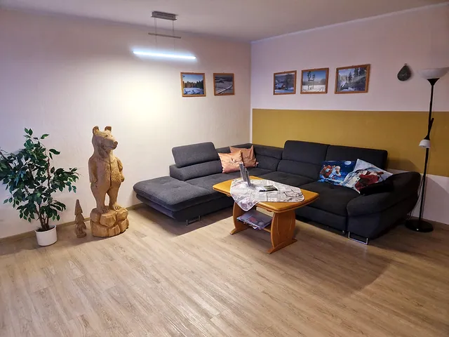 Wohnzimmer mit großer grauer Eckcouch, Couchtisch und geschnitztem Holzbären